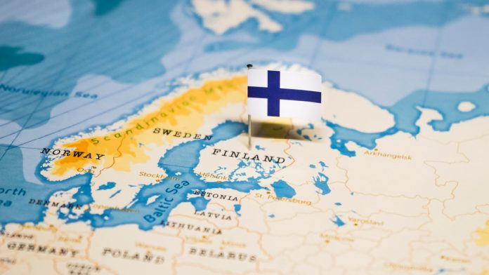 Finland flag sticking out of a paper world map.
