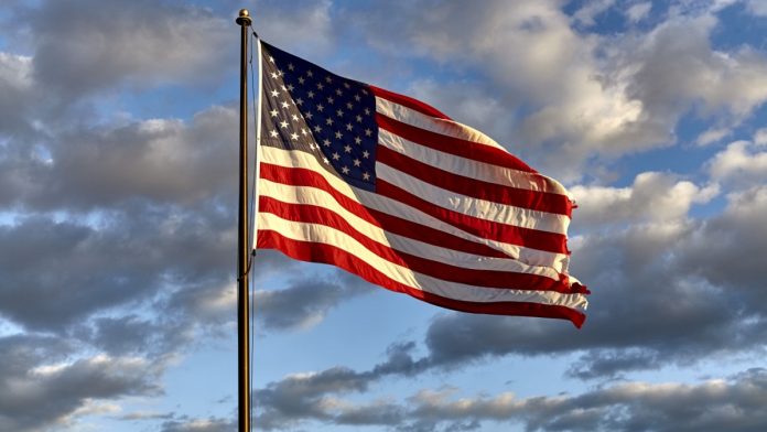 American flag on flagpole waving in the wind against clouds, blue sky and the moon.