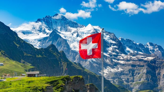 Swiss flag waving and tourists admire the peaks of Monch and Jungfrau mountains on a Mannlichen viewpoint, Bernese Oberland Switzerland.