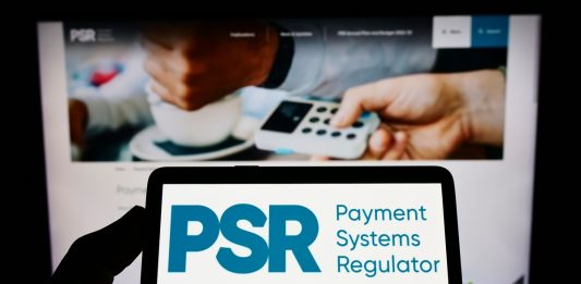 Person holding mobile phone with logo of British Payment Systems Regulator (PSR) on screen in front of business web page.