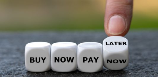 Hand turns dice and changes the expression 'buy now pay now' to 'buy now pay later'.