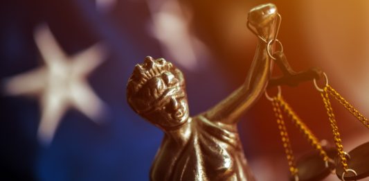 Law and Justice in United States of America, statue of Lady Justice with USA flag in background, selective focus.