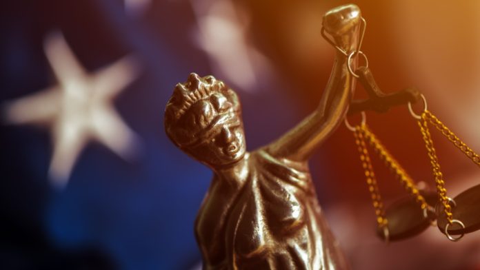 Law and Justice in United States of America, statue of Lady Justice with USA flag in background, selective focus.