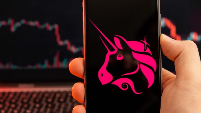 Uniswap UNI cryptocurrency logo on the screen of smartphone in mans hand with downtrend on the chart on a red light background, February 2022, San Francisco, USA.