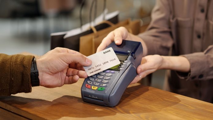 Hand of unrecognizable male consumer holding credit card over terminal screen during contactless payment while standing by counter.