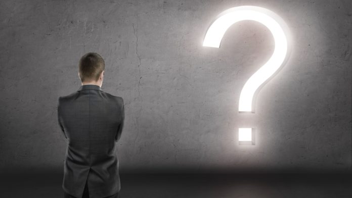 Businessman standing in front of concrete wall with bright big question mark. Financial and business concept.