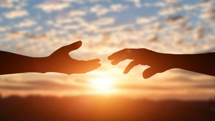 Silhouette of reaching, giving a helping hand, hope and support each other over sunset background.