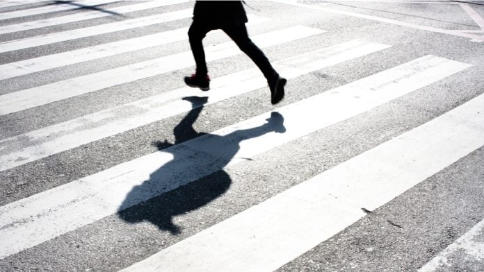 Blurry child's legs and kid's shadow with a backpack, on crossing while running over the street.