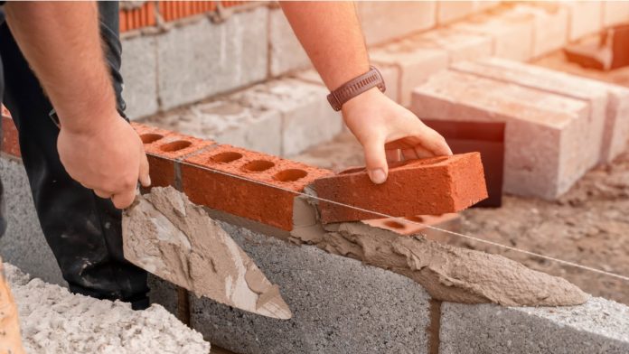 Bricklayer laying brick on cement mix on construction site close-up. Reduce the housing crisis by building more affordable houses concept.