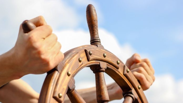 Steering hand wheel ship on sky background, hand hold hand wheel.