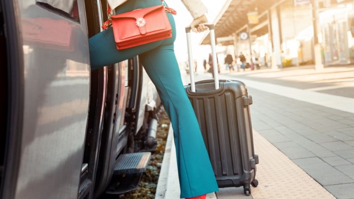 Legs's close up of a business woman getting on the train with bag and trolley bag.