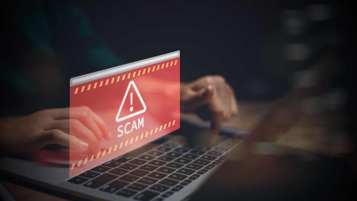 A man types on a laptop keyboard as a fraud scam pop up appears