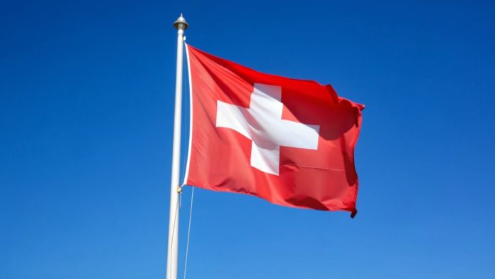 Swiss flag flying in the wind blue sky, copyspace. swiss flag in the wind in front of a blue sky sunshine during the day. light veil clouds. direct democracy and freedom. sunshine during the day.