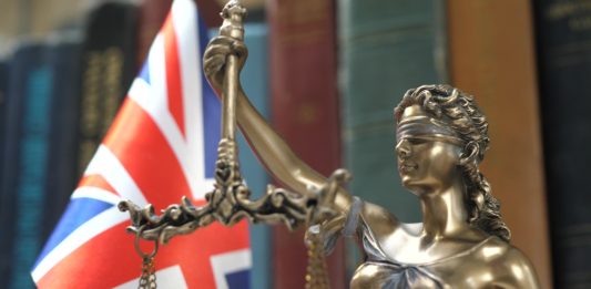 Statue of Lady Justice with Bookshelf with Books and United Kingdom Flag Background. Tribunal and justice concept. Consultation with insurance lawyer and customer.