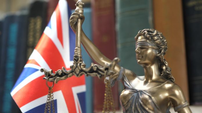 Statue of Lady Justice with Bookshelf with Books and United Kingdom Flag Background. Tribunal and justice concept. Consultation with insurance lawyer and customer.