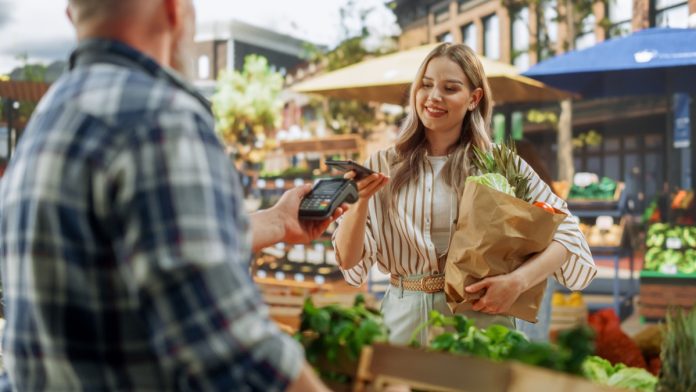A merchant offering a POS terminal to a shopper at a market