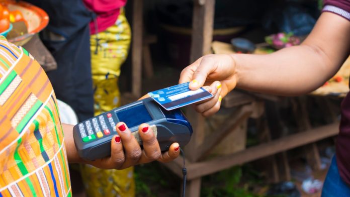 African market women making transition with Point of sale machine and a Credit card. Woman paying bills online using bank card in a local market.