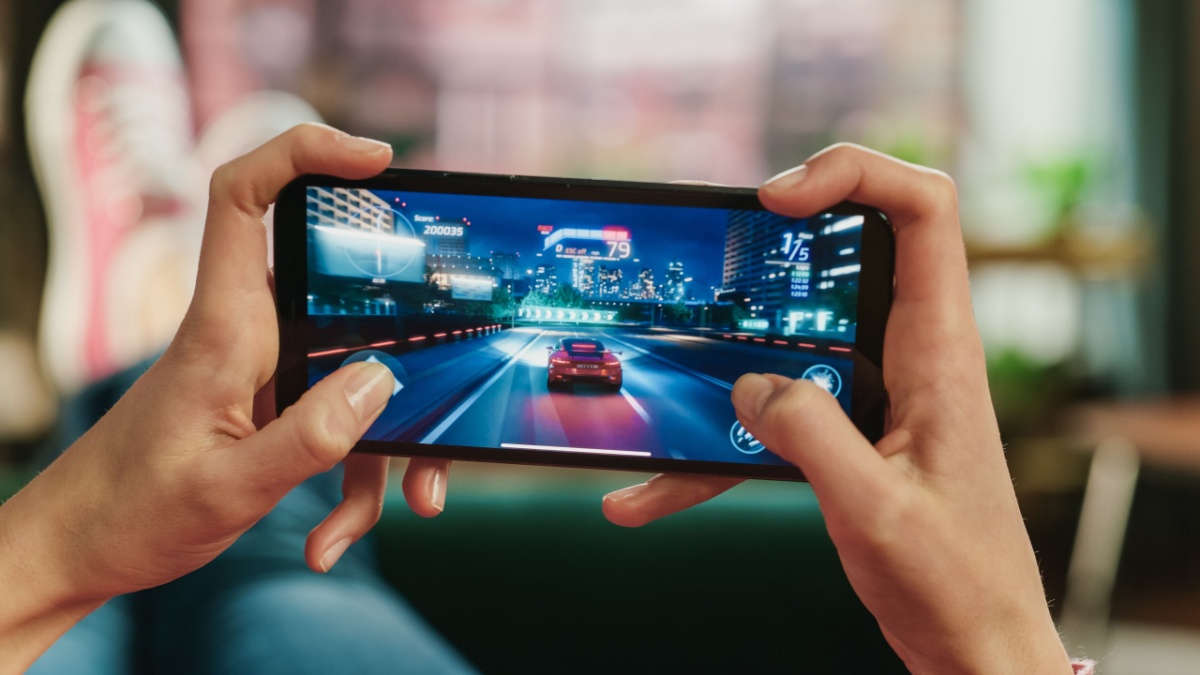 Paytently Q&A on iGaming visualised by Female is Relaxing on a Couch at Home, Playing an Interactive Racing Drift Video Game on Her Smartphone. Gamer Lies on a Sofa in Living Room. Close Up POV Photo of Mobile Device Screen.