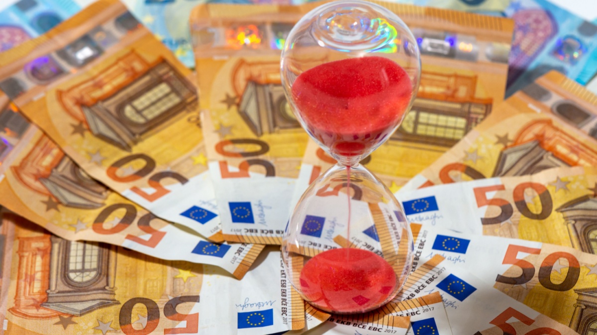 An image of an hourglass in a stack of euro notes representing T+1 settlement