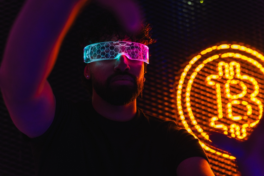 Man wearing futuristic smart glasses using augmented reality in front of bitcoin logo. Relates to crypto gaming.