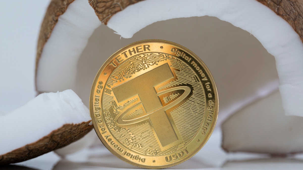 Tether USDT cryptocurrency physical coin placed next to broken coconut on the white reflective table. Macro shot.