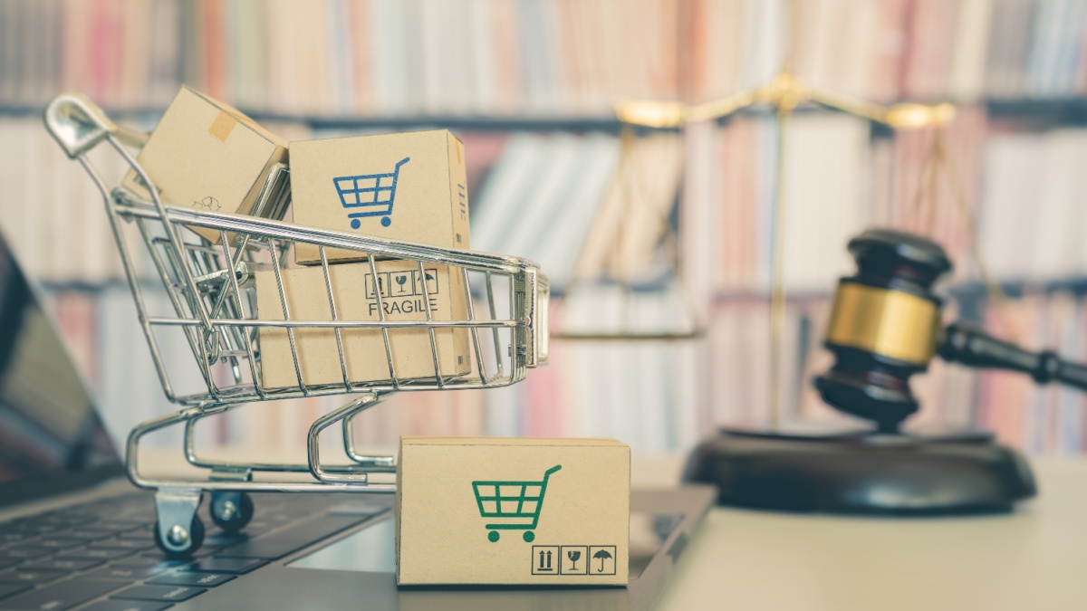Consumer rights and consumer protection, business law concept : Shopping basket, shopping boxes and a shopping cart on a laptop computer with judge gavel, balance sale of justice and bookshelf behind.