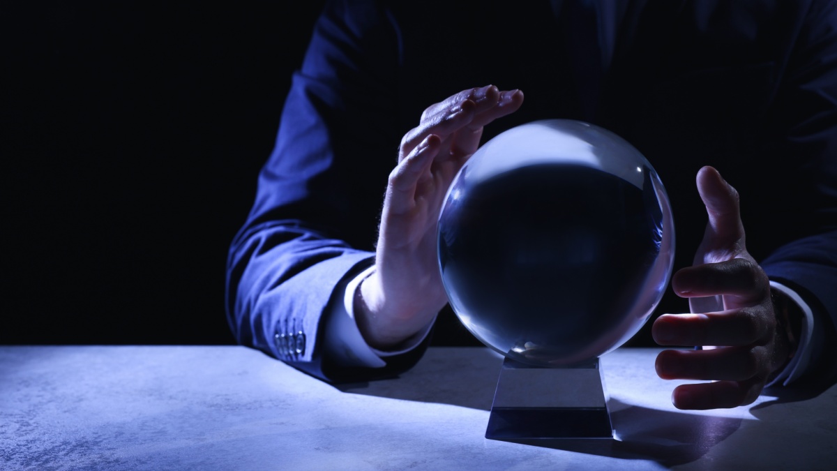 Businessman using crystal ball to predict future at table in darkness, closeup. Space for text.