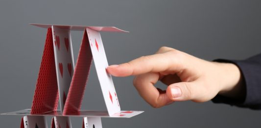 Woman destroying house of playing cards on grey background, closeup.