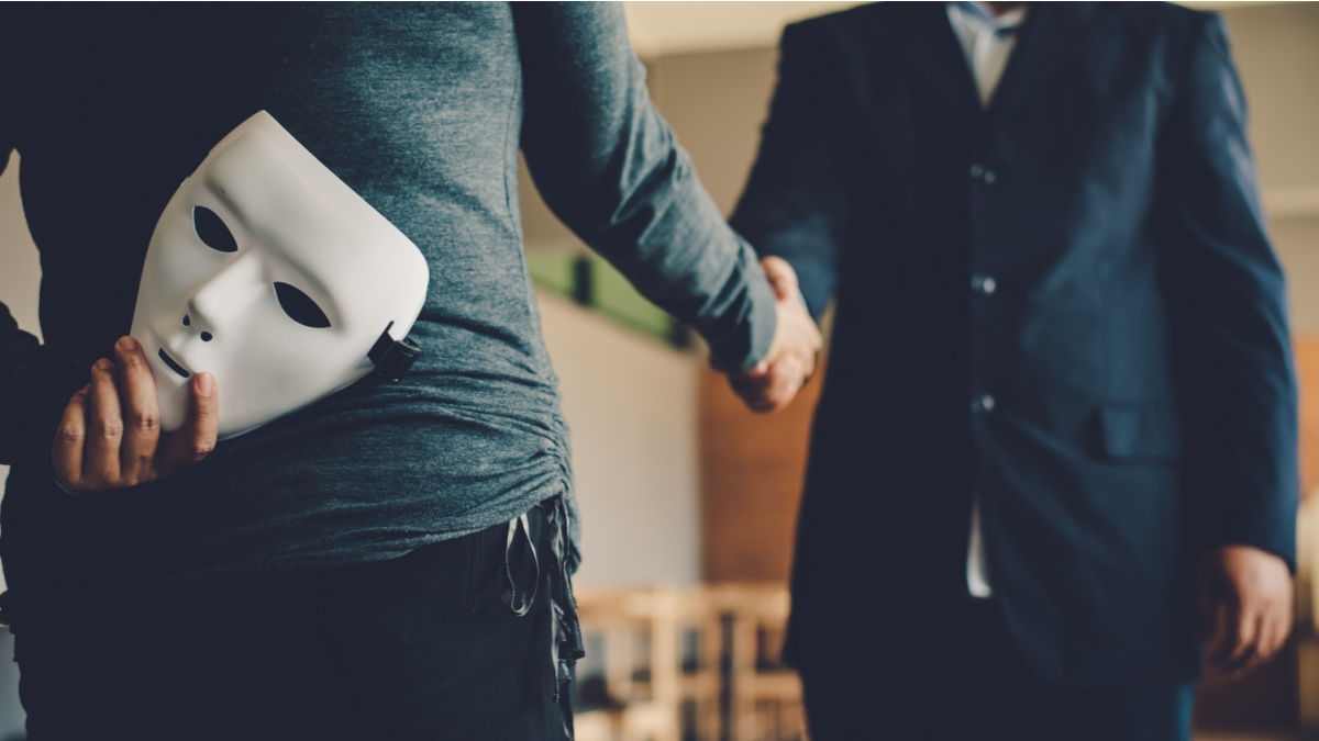 Fraudster shaking hands with a man, while holding a white mask behind his back.