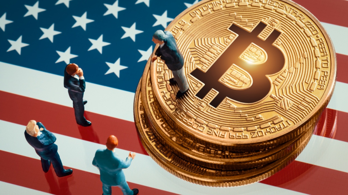 Miniature businessman figurines standing near the pile of shiny golden crypto on US flag.