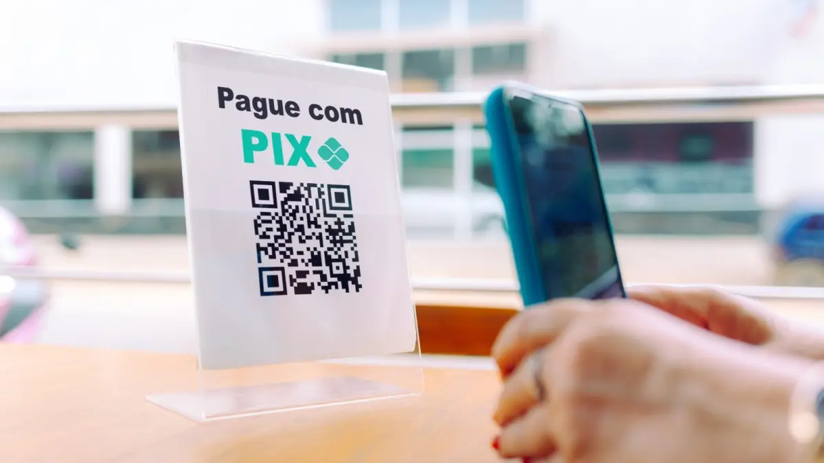 Hands holding a smartphone scanning a QR code on an acrylic stand for payment via PIX.