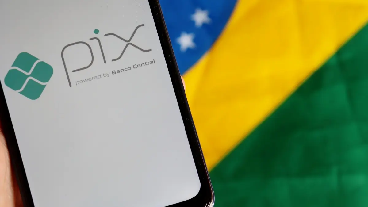 Hand holding smartphone with Pix logo on screen with Brazilian flag in the background. Pix is the new instant payment system from Central Bank of Brazil.